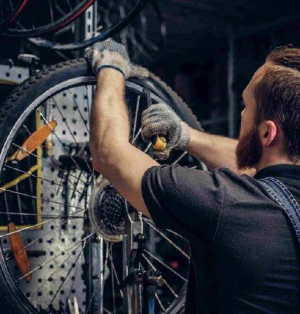 bearded-mechanic-repairing-bicycle-wheel-tire-in-workshop-back-view-service-manualWEBP_11zon-1-640x427